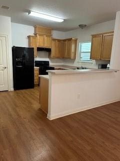 kitchen with light countertops, a peninsula, wood finished floors, and black appliances