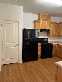 kitchen with wood finished floors, light countertops, under cabinet range hood, and black appliances