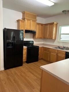 kitchen featuring a sink, light countertops, light wood-type flooring, under cabinet range hood, and black appliances