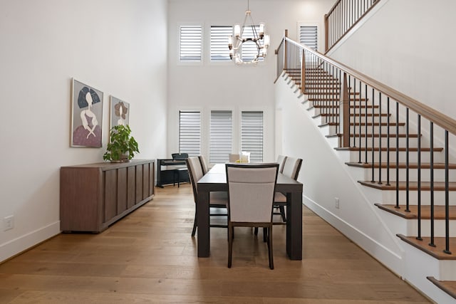 dining room with a high ceiling, a chandelier, baseboards, wood finished floors, and stairway