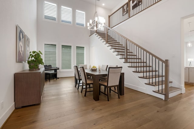 dining area featuring stairs, a high ceiling, a notable chandelier, and hardwood / wood-style flooring