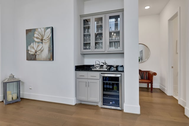 bar with wine cooler, baseboards, indoor wet bar, and light wood-style flooring