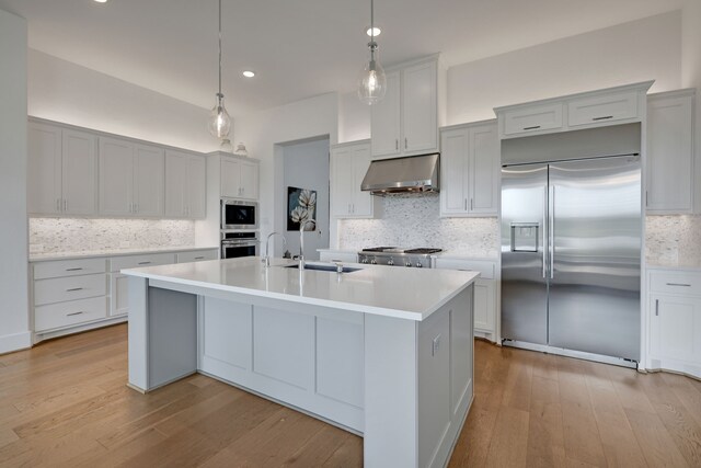 kitchen with built in appliances, light countertops, under cabinet range hood, and tasteful backsplash