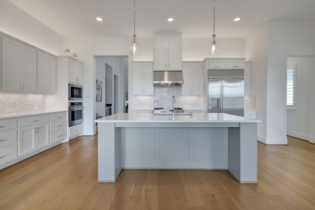 kitchen with built in appliances, under cabinet range hood, decorative backsplash, and light countertops