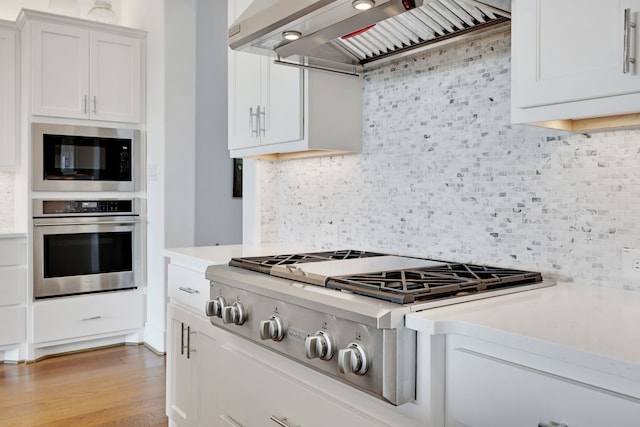 kitchen featuring custom range hood, light countertops, appliances with stainless steel finishes, and tasteful backsplash