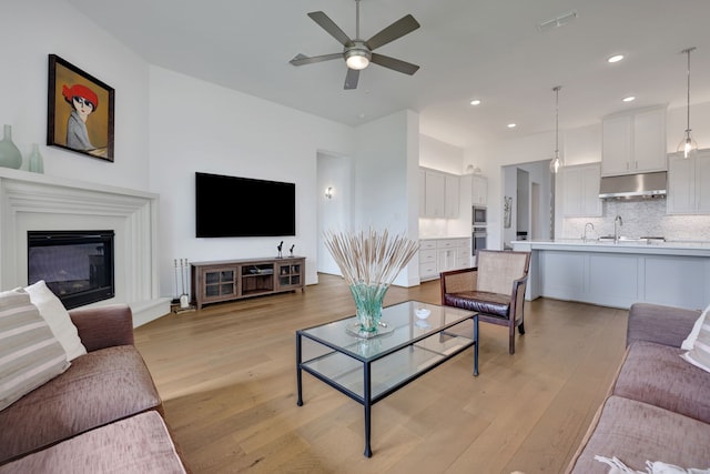 living area with light wood-type flooring, recessed lighting, a glass covered fireplace, and ceiling fan