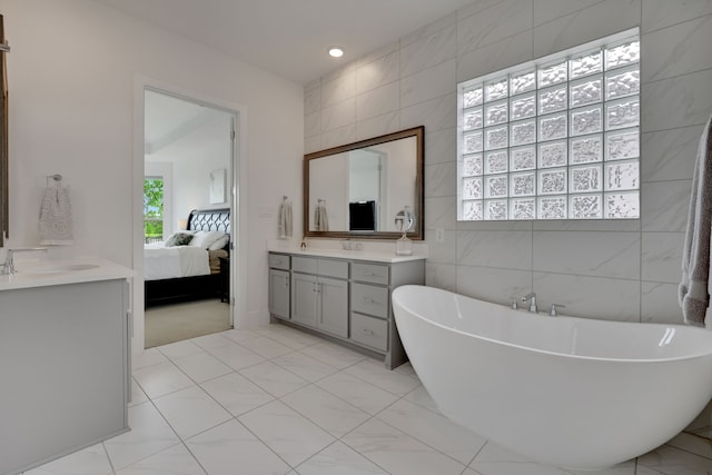 bathroom featuring a freestanding tub, tile walls, vanity, connected bathroom, and recessed lighting