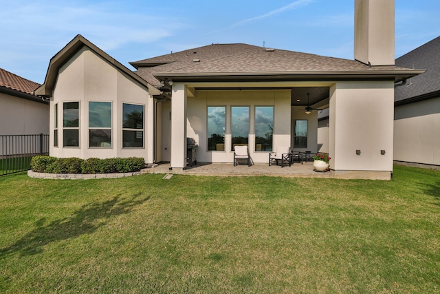 back of house with a ceiling fan, a patio area, a yard, a shingled roof, and stucco siding