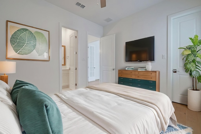 bedroom with a ceiling fan, ensuite bath, wood finished floors, and visible vents