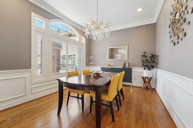 dining space with a notable chandelier, ornamental molding, wood finished floors, and a wainscoted wall