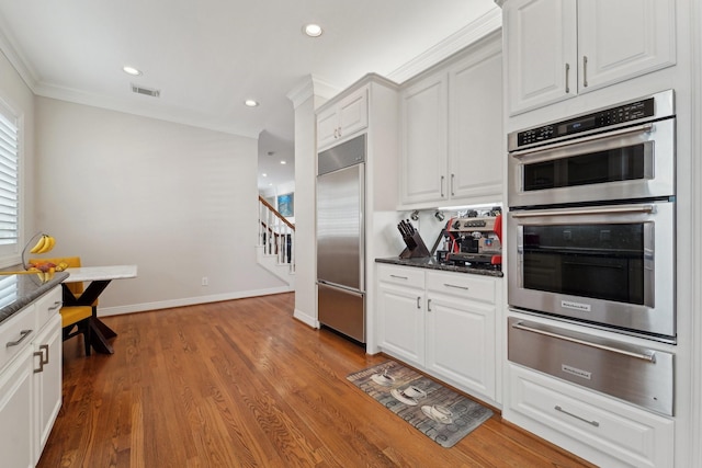 kitchen with visible vents, wood finished floors, a warming drawer, ornamental molding, and stainless steel appliances