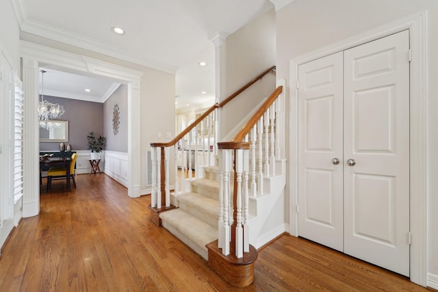 stairway featuring crown molding, a notable chandelier, a decorative wall, a wainscoted wall, and wood finished floors