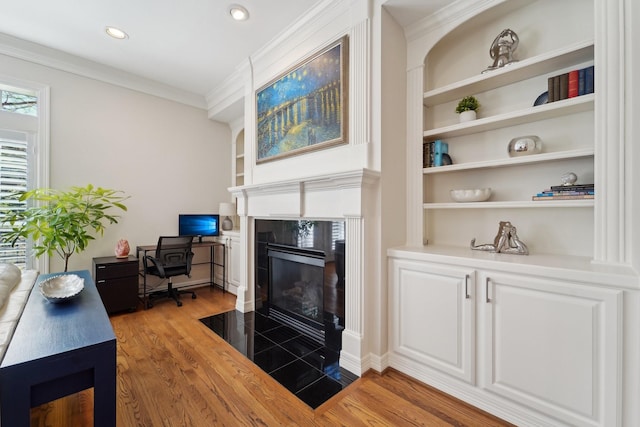 living area with ornamental molding, built in features, wood finished floors, and a fireplace
