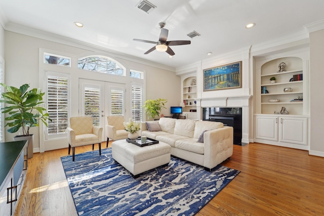 living room featuring crown molding, a premium fireplace, a ceiling fan, light wood-type flooring, and visible vents