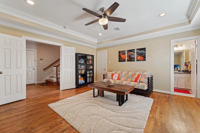 living room featuring visible vents, stairs, ceiling fan, light wood-type flooring, and a tray ceiling