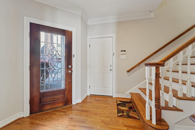 foyer entrance featuring crown molding, stairway, baseboards, and light wood finished floors