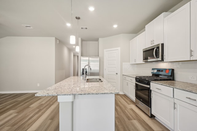 5030 Magnolia Springs Dr, Pearland, TX 77584 - kitchen featuring appliances with stainless steel finishes, a sink, light wood finished floors, tasteful backsplash, and a center island with sink