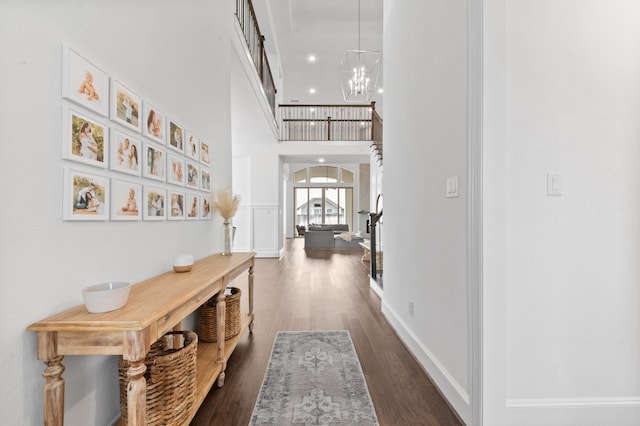 hall featuring an inviting chandelier, a towering ceiling, baseboards, dark wood-type flooring, and recessed lighting