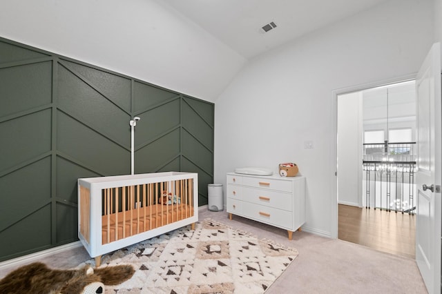 bedroom with light carpet, a decorative wall, baseboards, lofted ceiling, and visible vents