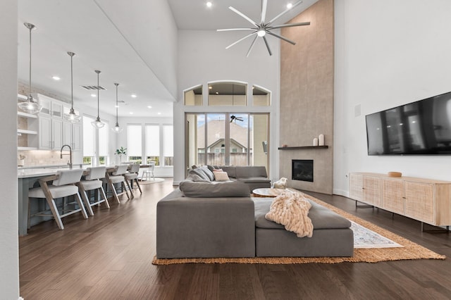 living room featuring dark wood-style flooring, ceiling fan, a high ceiling, and a fireplace