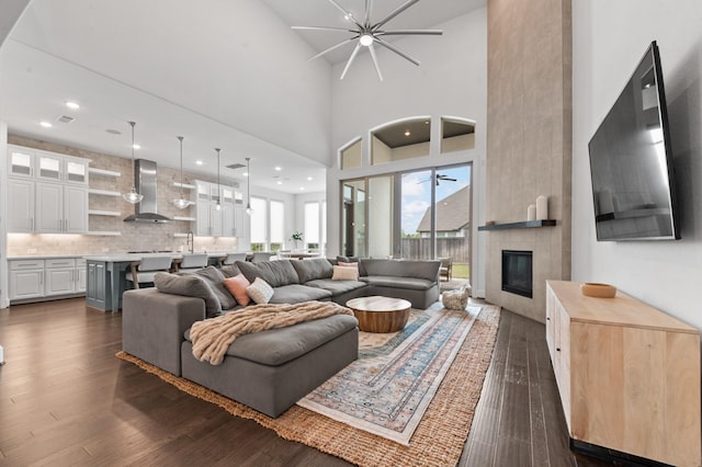 living area with a tiled fireplace, dark wood-style flooring, and ceiling fan