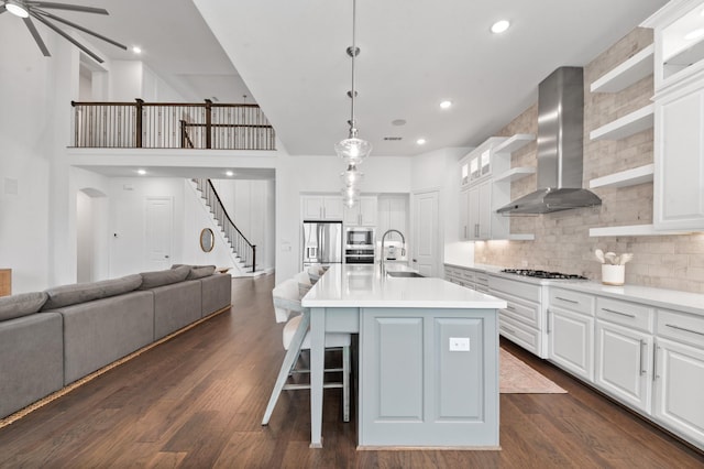 kitchen featuring open shelves, wall chimney range hood, light countertops, a sink, and backsplash