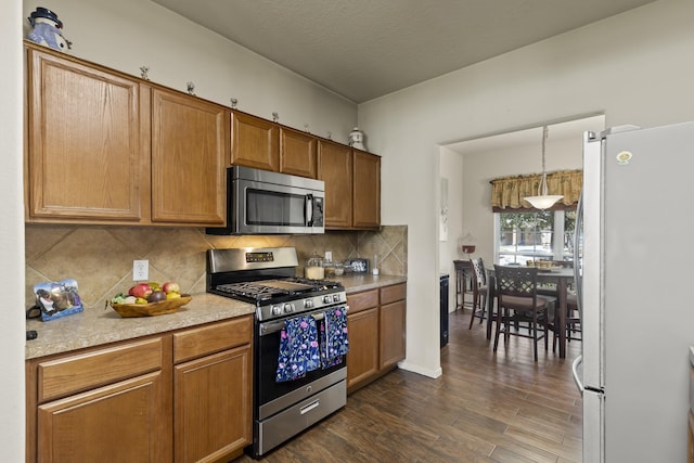 kitchen featuring decorative backsplash, brown cabinetry, dark wood-style flooring, appliances with stainless steel finishes, and light countertops