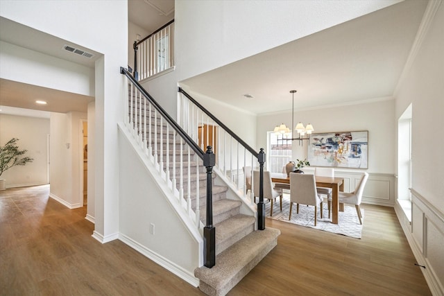 stairway with crown molding, a chandelier, visible vents, and wood finished floors