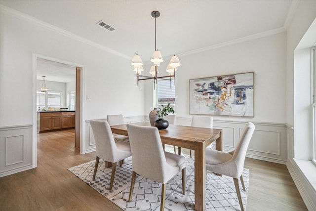 dining area with visible vents, crown molding, wainscoting, light wood finished floors, and a chandelier