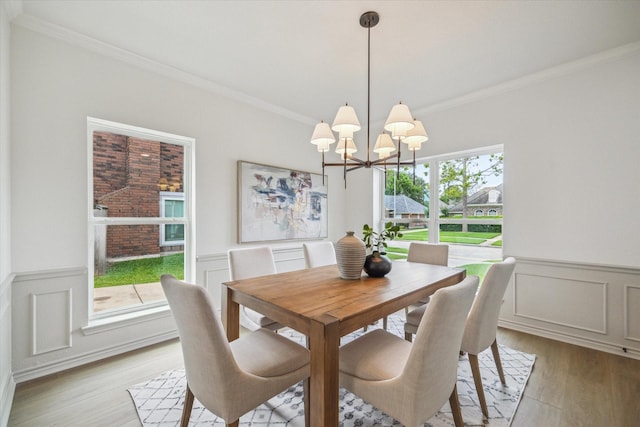 dining room with crown molding, an inviting chandelier, wainscoting, and light wood-type flooring