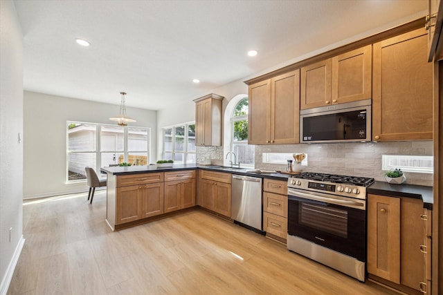 kitchen with backsplash, appliances with stainless steel finishes, dark countertops, a sink, and light wood-style floors
