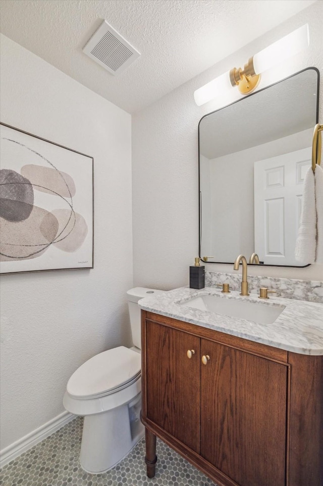 half bathroom featuring visible vents, baseboards, toilet, and vanity