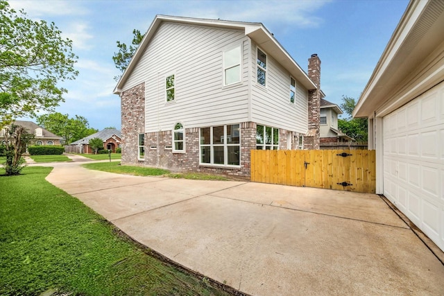 back of house featuring fence, brick siding, a garage, a lawn, and driveway
