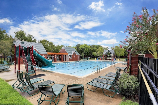 pool with a patio area, a water slide, playground community, and fence