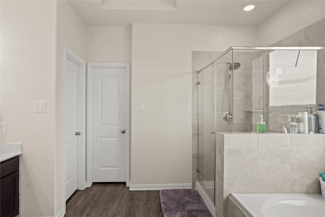 bathroom with a bath, a shower stall, wood finished floors, vanity, and baseboards