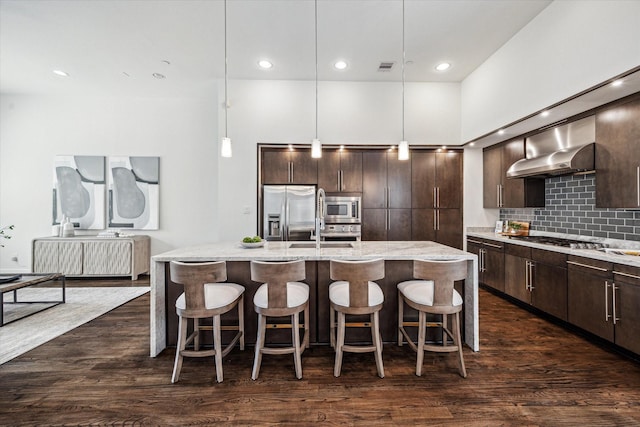 kitchen featuring a kitchen island with sink, backsplash, dark wood-style flooring, dark brown cabinets, and stainless steel appliances