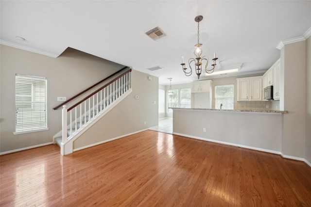 unfurnished living room with crown molding, a chandelier, baseboards, light wood-type flooring, and stairway