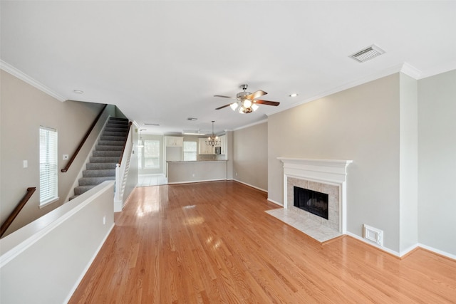 unfurnished living room with ornamental molding, light wood-type flooring, a tile fireplace, and visible vents