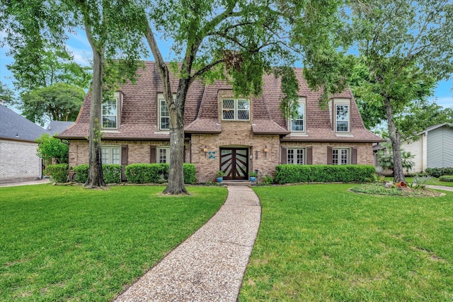 view of front of home with brick siding, a shingled roof, french doors, and a front yard