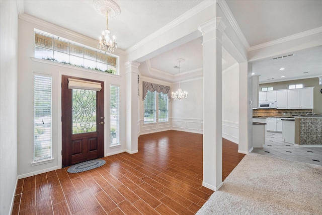 entryway featuring ornamental molding, decorative columns, and a notable chandelier