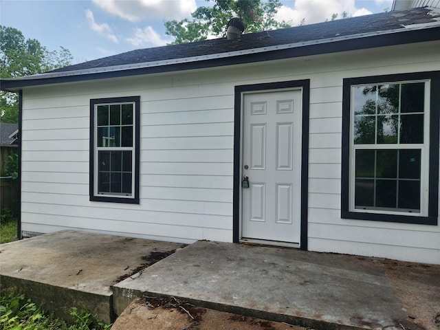 view of exterior entry featuring a patio and a shingled roof