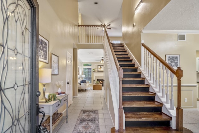 entryway with a ceiling fan, a high ceiling, tile patterned floors, visible vents, and stairway