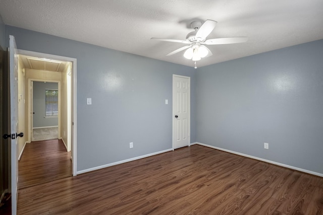 unfurnished room featuring attic access, dark wood finished floors, baseboards, and ceiling fan