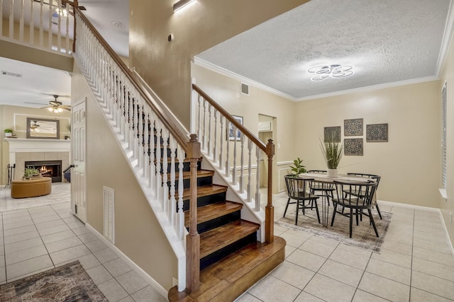 staircase with ornamental molding, visible vents, tile patterned floors, a ceiling fan, and a tile fireplace