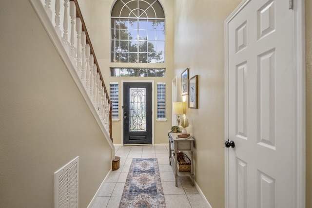 entrance foyer featuring baseboards, visible vents, light tile patterned flooring, a towering ceiling, and stairway