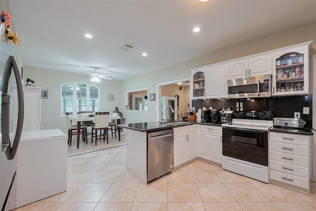 kitchen featuring visible vents, a peninsula, dark countertops, a sink, and appliances with stainless steel finishes