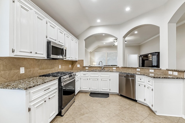 kitchen featuring lofted ceiling, white cabinets, a sink, dark stone countertops, and stainless steel appliances