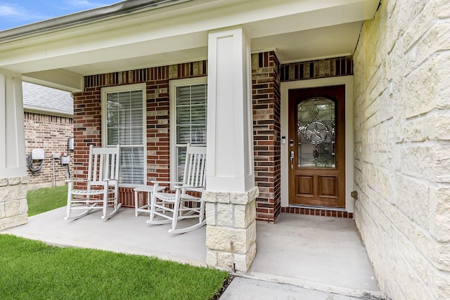 view of exterior entry featuring a porch and brick siding
