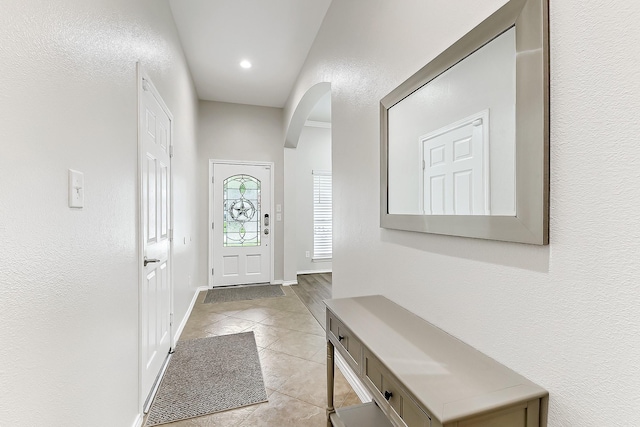 doorway to outside featuring arched walkways, baseboards, recessed lighting, and light tile patterned floors