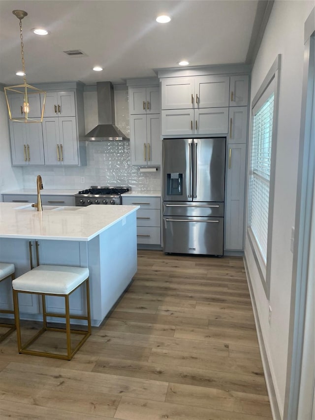 kitchen with wall chimney range hood, gray cabinets, stainless steel refrigerator with ice dispenser, range, and light countertops